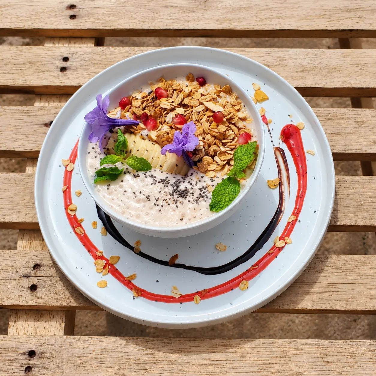 Tropical breakfast bowl with granola, banana, pomegranate, mint and edible flowers
